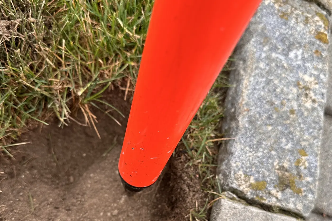 An orange prism pole tip set on a point in the soil beside a granite cobblestone edging